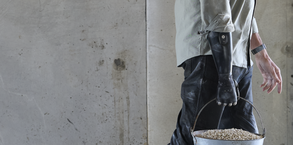 TASKA Hand and PowerCore user with dusty prosthesis carrying a bucket.